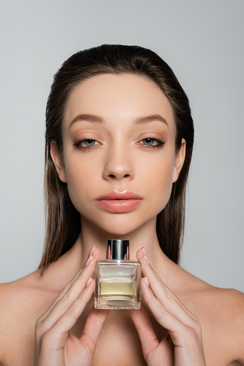 young woman with blue eyes holding bottle with luxury perfume isolated on grey
