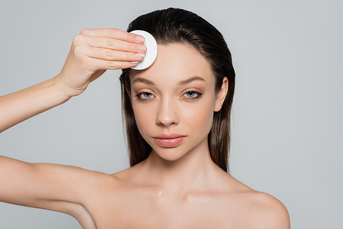 young woman removing makeup on forehead with soft cotton pad isolated on grey