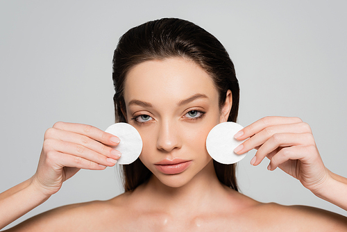 young woman removing makeup with cotton pads isolated on grey