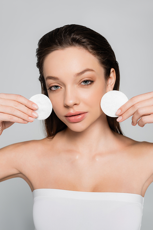 pretty young woman removing makeup with cotton pads isolated on grey