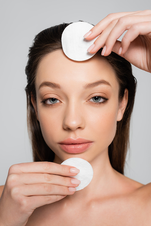 close up view of young woman removing makeup with cotton pads isolated on grey