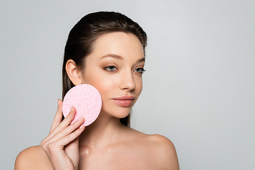 young woman with bare shoulders holding exfoliating sponge isolated on grey