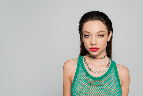 young and stylish model with red lips and necklaces posing isolated on grey