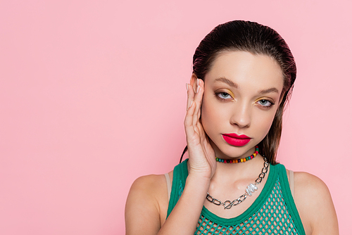 brunette woman with bright makeup posing while looking at camera isolated on pink