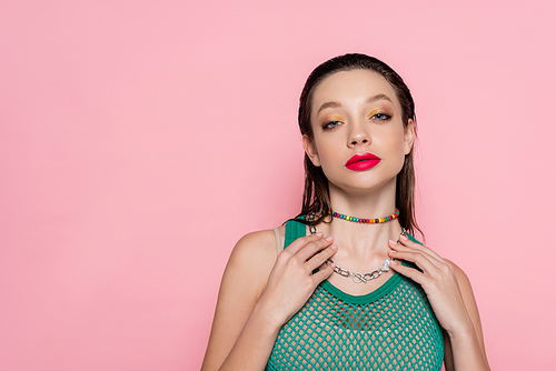young brunette woman with makeup posing and looking at camera isolated on pink