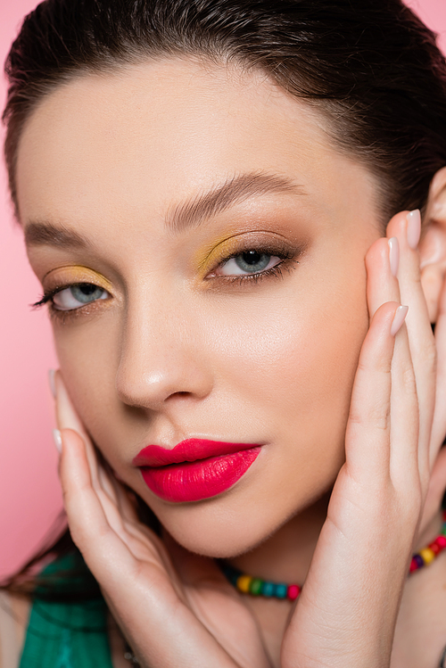 close up of young model with bright makeup looking at camera isolated on pink