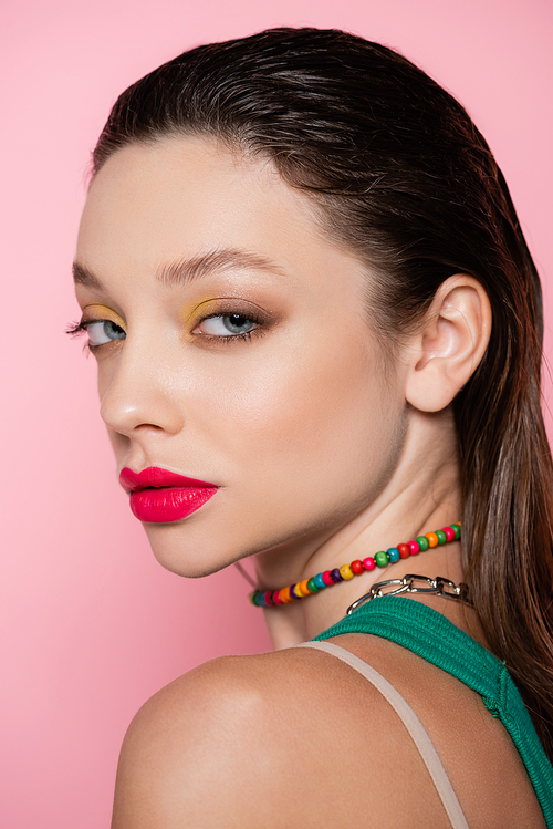 young brunette model with bright red lips posing while looking at camera isolated on pink