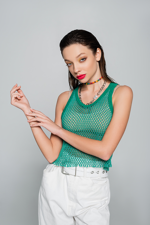 trendy woman in green tank top and colorful necklace posing isolated on grey