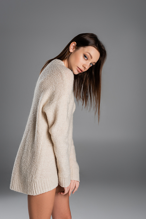 brunette woman in long and soft sweater looking at camera on grey background