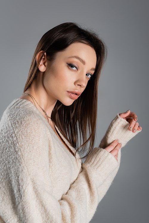 charming woman in warm sweater looking at camera isolated on grey