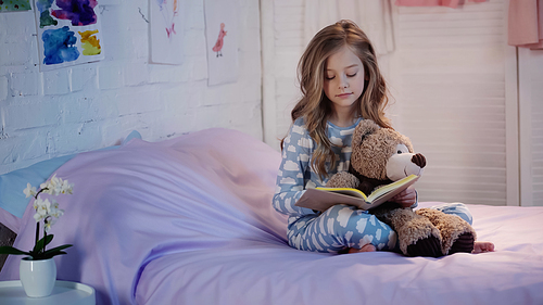 Preteen kid holding soft toy and reading book on bed