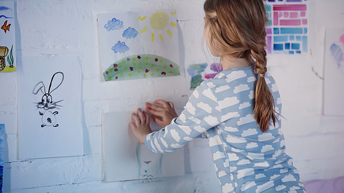 Preteen girl in pajama fastening painting on wall at home