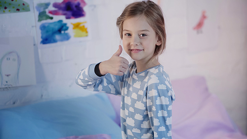 Smiling preteen child in pajama showing like gesture on bed at home