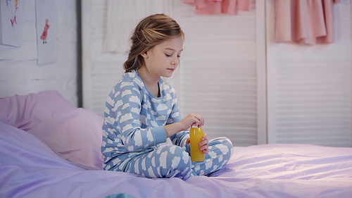 Preteen child in pajama holding bottle with orange juice on bed