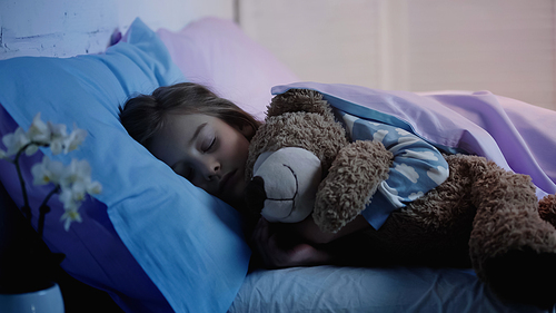 Preteen kid hugging soft toy while sleeping on bed at home