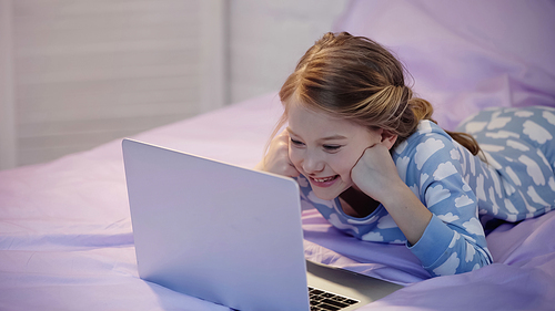 Happy kid in pajama looking at laptop in bedroom in evening
