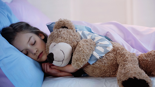 Child in pajama sleeping with soft toy at home