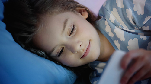 Smiling preteen child looking at blurred smartphone on bed