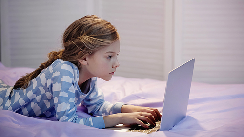 Preteen child in pajama using laptop while lying on bed at home