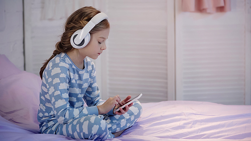 Side view of child in headphones using cellphone on bed
