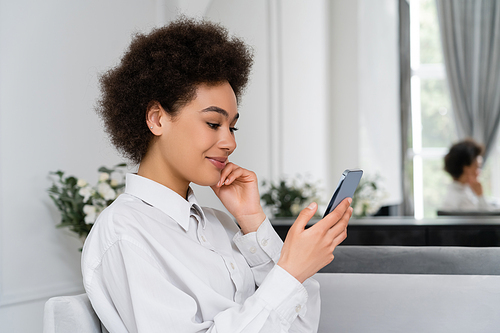 joyful african american woman smiling while using smartphone at home