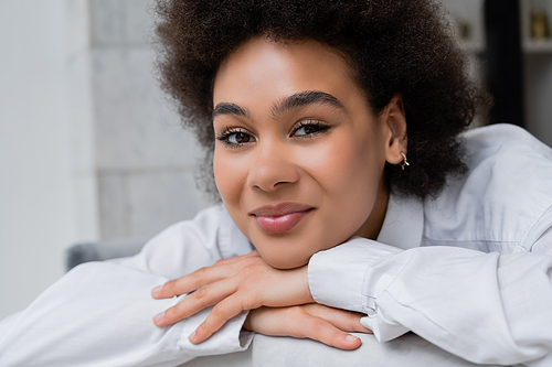 portrait of pleased and curly african american woman in white shirt with collar