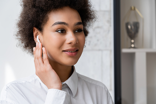 portrait of happy african american woman listening music and adjusting wireless earphone