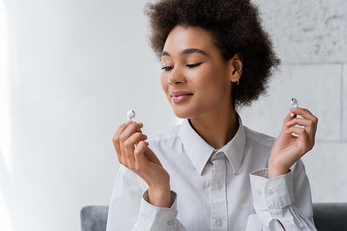 happy african american woman listening music and looking at wireless earphone