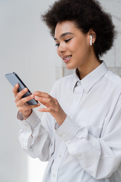 happy african american woman listening music in wireless earphone and using smartphone