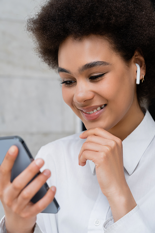 close up of happy african american woman listening music in wireless earphone and using smartphone