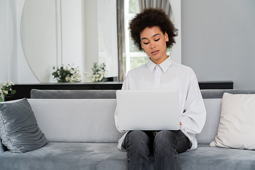 african american woman using laptop while working from home in modern living room