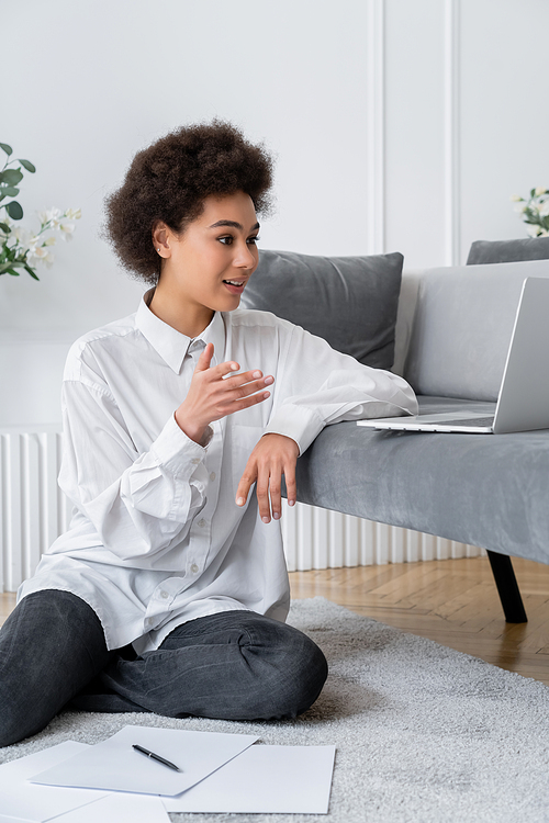 curly african american woman gesturing during video call in living room