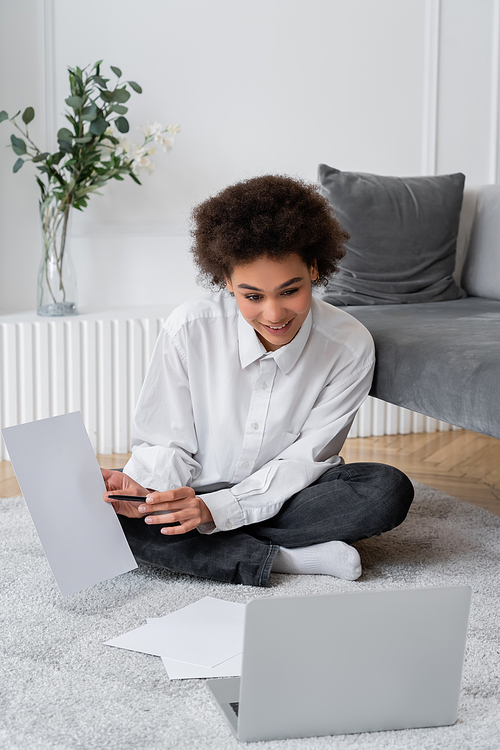 curly african american woman showing blank document during video call on laptop