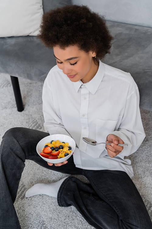 high angle view of african american woman holding bowl with corn flakes and berries