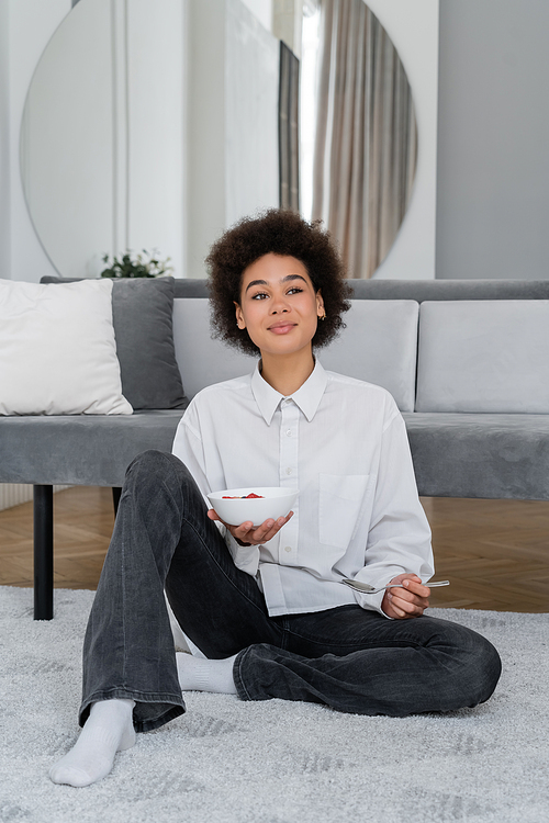 happy and young african american woman holding bowl with tasty breakfast