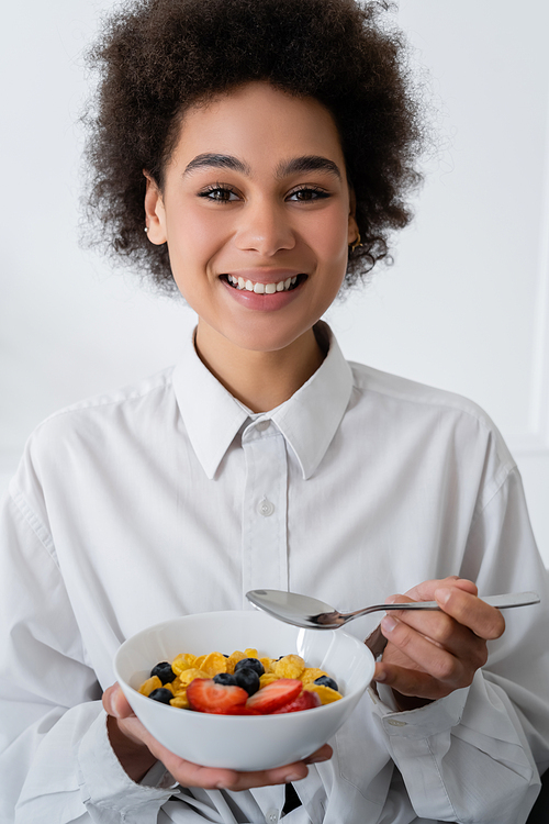 cheerful african american woman holding bowl with corn flakes and berries