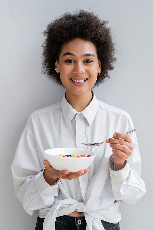 young and cheerful african american woman holding bowl with tasty breakfast on white