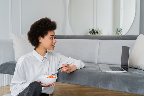 side view of curly african american woman watching movie while having breakfast in living room