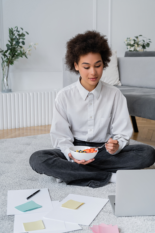 curly african american freelancer looking at laptop while having breakfast at home