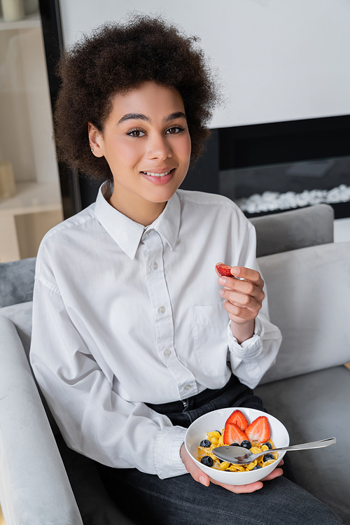 happy african american woman holding bowl with corn flakes and fresh strawberry