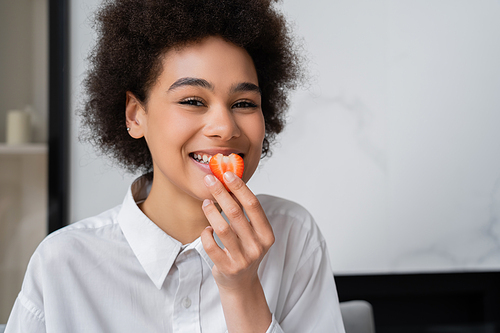 happy african american woman eating fresh strawberry and looking at camera