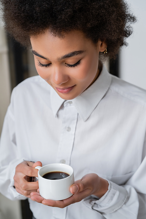 curly african american woman in white shirt looking at cup of coffee