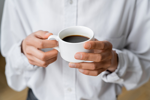 cropped view of woman holding cup of black and hot coffee in hands