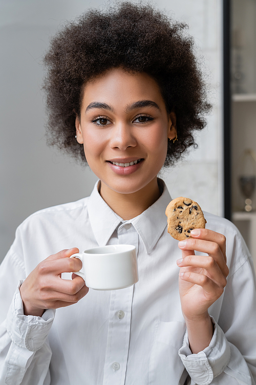 happy african american woman holding cup of coffee and cookie with chocolate chips