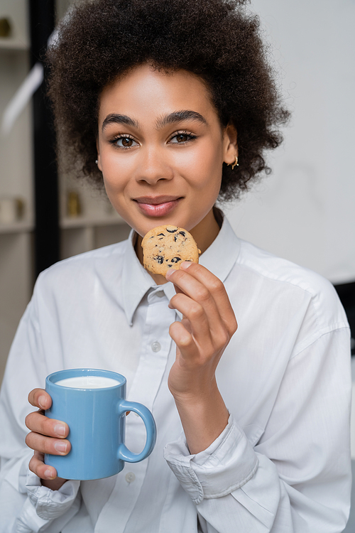 cheerful african american woman holding cup of milk and cookie with chocolate chips