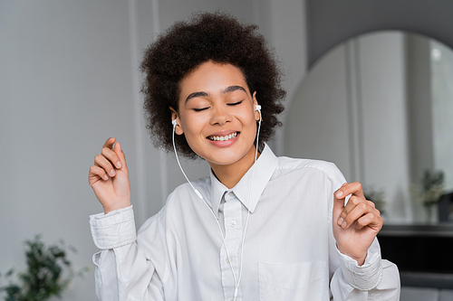 cheerful african american woman with closed eyes listening music in wired earphones