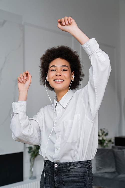 cheerful african american woman listening music in wired earphones and dancing at home