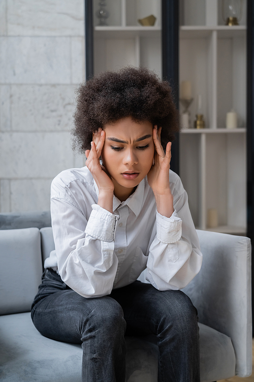 stressed african american woman in white shirt sitting in living room