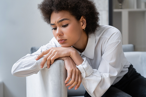 frustrated african american woman in white shirt sitting in living room