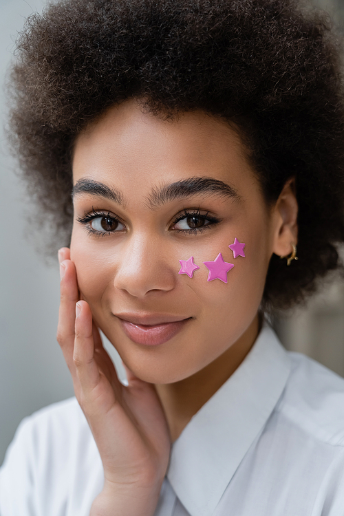 portrait of smiling african american woman with decorative purple stars on cheek
